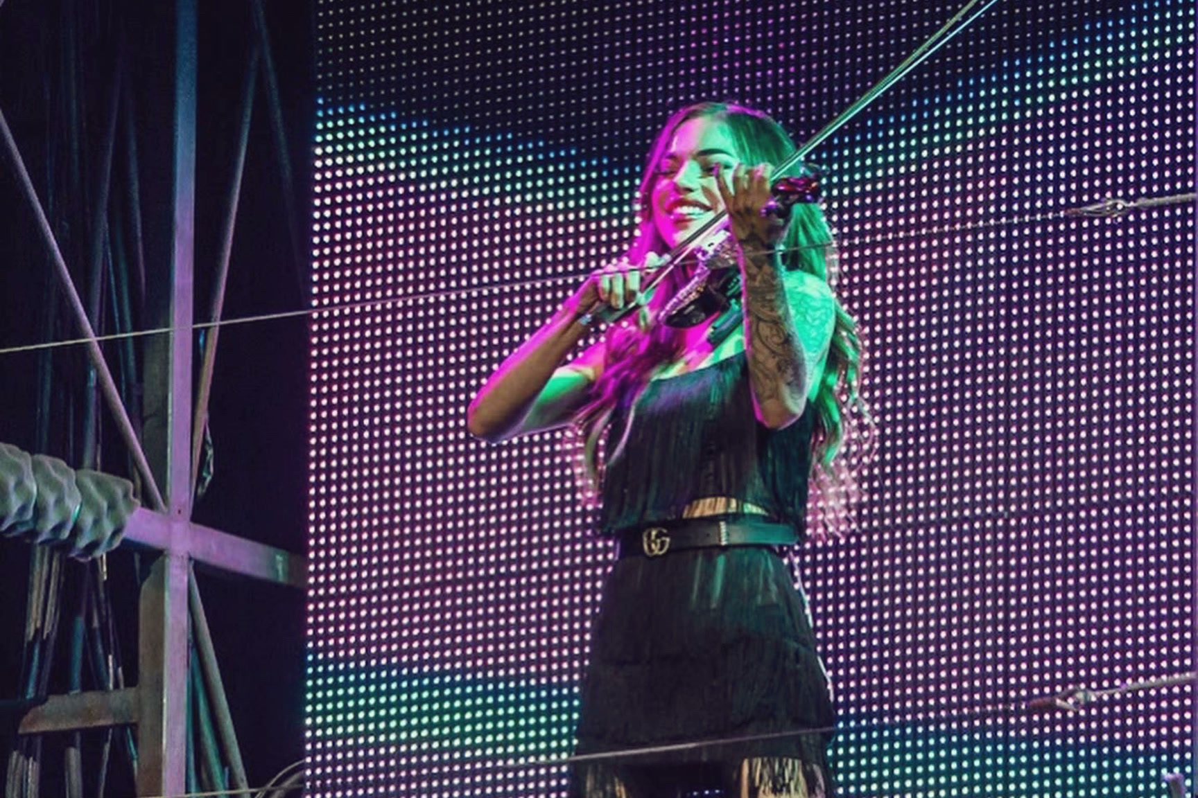 A violinist playing on stage in front of a wall of lights