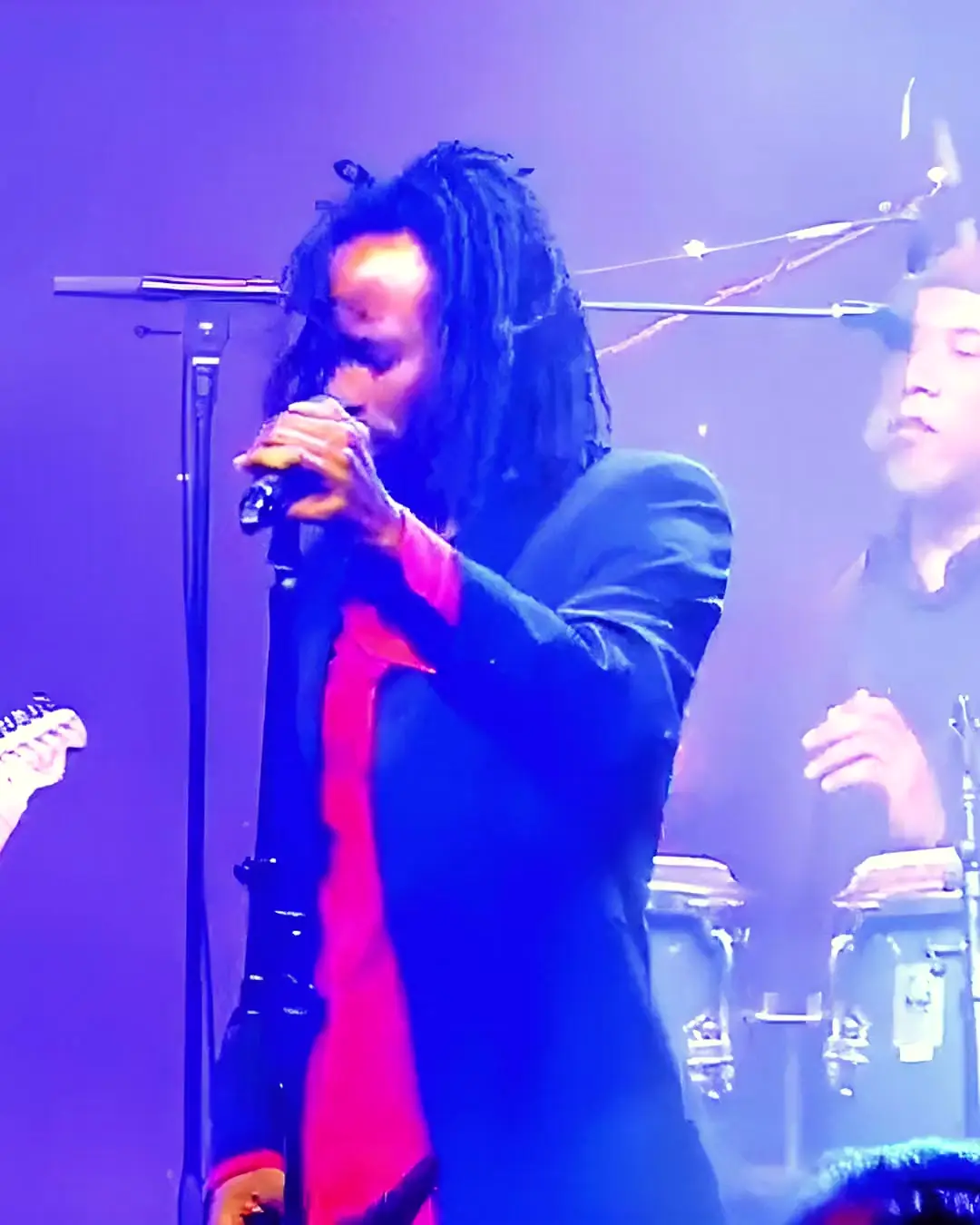 A singer at the microphone on a stage strung with coloured lights, the band behind him